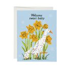 A square greeting card with a light blue background, featuring an illustration of a white goose and yellow daffodils, with the text 'Welcome sweet baby' at the top. A white envelope is partially visible behind the card.