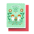 A greeting card with a mint green background and a pink envelope behind it. The card features a whimsical illustration of two white characters wearing orange mushrooms and holding a basket, surrounded by smiling flowers, with the text 'CONGRATS on your Little Button'.