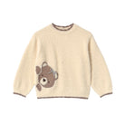 A cream-colored fuzzy long-sleeve sweater with a brown teddy bear face motif on the left chest and brown trim on the collar, cuffs, and hem.