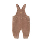 A baby's corduroy overall romper in a warm taupe-brown color, featuring adjustable shoulder straps with snap buttons and front patch pockets, shown against a plain white background.