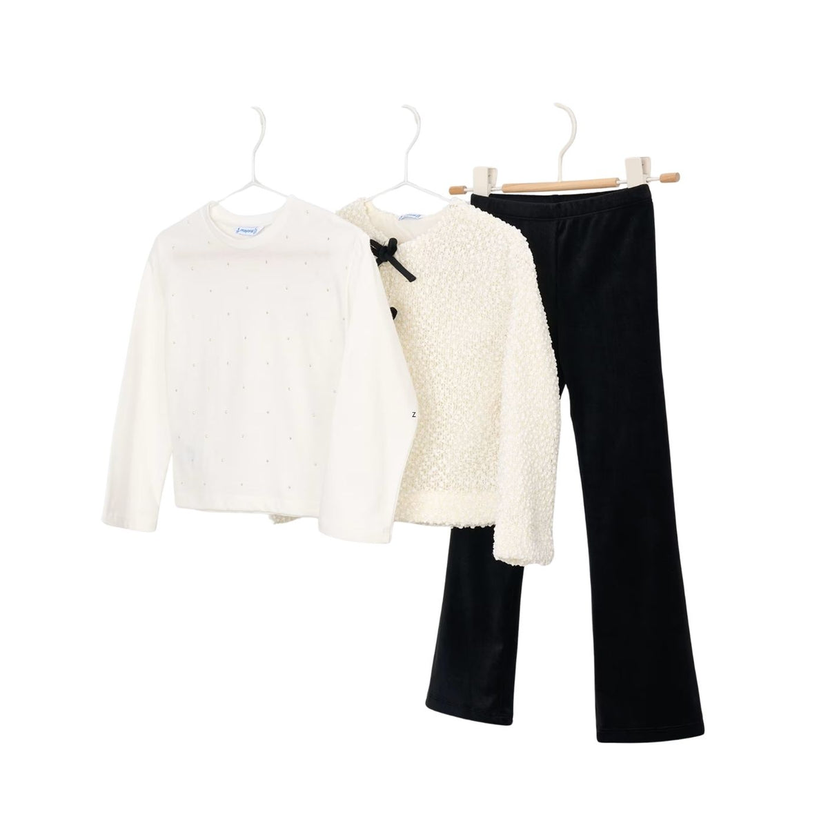 A three-piece girls' clothing set displayed on hangers against a white background, featuring a white long-sleeve top with tiny dot patterns, a cream textured jacket with a black bow detail, and black pants.