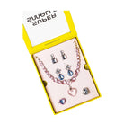 A pink and silver jewelry set displayed inside a bright yellow box. The set includes a beaded necklace with blue teardrop and heart charms, matching stud earrings, and several small charm links on a pale pink insert.