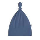 A dusty blue knit beanie hat with a knotted top and a small black brand tag on the side, shown against a plain white background.