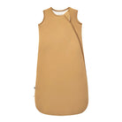A sleeveless baby sleep sack in a warm camel tan color, featuring a diagonal zipper and a small black tag near the bottom left hem, shown against a plain white background.