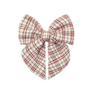 A decorative children's hair bow featuring a festive red, white, and tan plaid pattern with long, pointed tails.