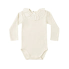 A long-sleeve baby bodysuit in a natural beige colorway, featuring a delicate ruffled collar and snap closures at the inseam, laid flat against a solid white background.