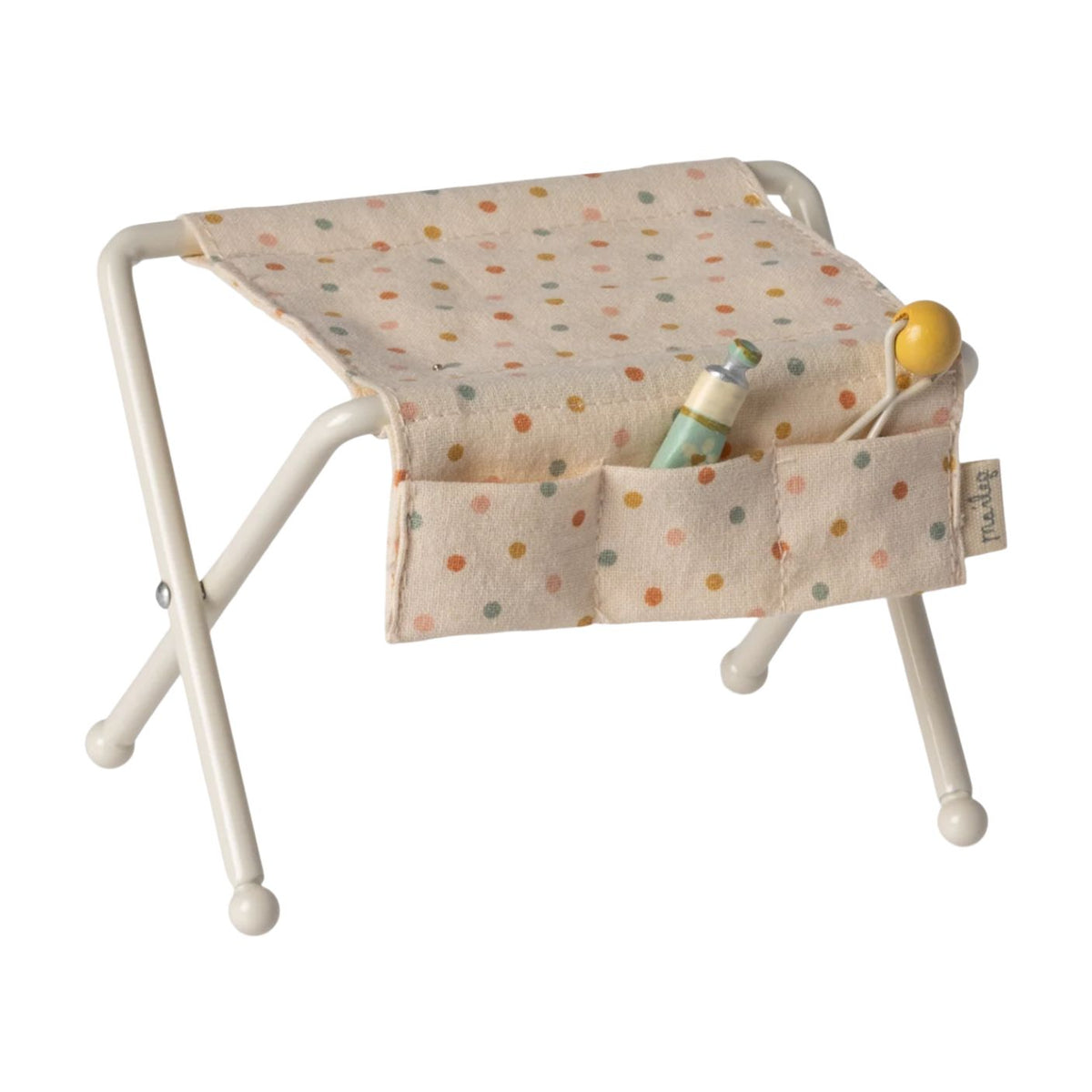 Maileg off-white miniature nursery changing table for baby mice, featuring metal folding legs, a polka-dot fabric changing pad, side pockets, a tiny rattle, and a baby lotion bottle.