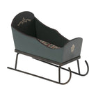 A miniature green wooden Maileg toy mouse sleigh with hand-painted floral decorations, a patterned fabric mattress inside, and dark metal runners.