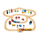 A complete wooden toy train set laid out on a white background, featuring a figure-eight track configuration. A blue train engine with several yellow and blue cargo cars is positioned on the tracks alongside a red toy car and a delivery truck. The scene is decorated with various colorful wooden town elements, including houses, trees, traffic lights, and a bridge crossing over the lower section of the track.