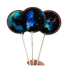 Three galaxy-themed lollipops on sticks held by a hand against a white background