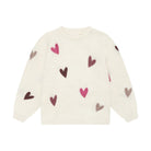 An off-white knit sweater with long sleeves, featuring an all-over pattern of small hearts in dark brown, pink, and light gray.