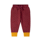 A pair of children's jogger pants in burgundy with a pattern of small orange dots, featuring a matching drawstring waist and contrasting mustard yellow ribbed cuffs.