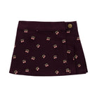 A dark plum corduroy mini skirt with an all-over cherry print and a single gold button closure on the right side, shown flat against a white background.