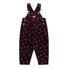 A pair of toddler boy's dark purple corduroy overalls with a small repeating pattern of cartoon faces, gold buttons, and adjustable shoulder straps, shown flat on a white background.