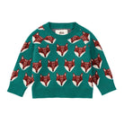 A front view of the Family Fox Sweater - Foxwood Fair Isle by Tea Collection, featuring an emerald green knit background patterned with rows of repeating, stylized red-and-white fox faces across the chest and sleeves, set against a plain white background.
