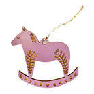 A pink wooden rocking horse ornament with engraved brown leaf and heart patterns, hanging from a twisted string on a white background.