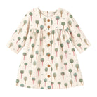 A long-sleeve baby dress with an all-over tree print on a cream-colored fabric, featuring brown buttons down the front and a gathered waist.