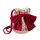 A small drawstring bag with a large red velvet bow, featuring a champagne gold sequined body and a matching red shoulder strap, shown on a plain white background.