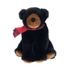 A black plush teddy bear with a brown snout, paw pads, and ear tips, wearing a red plaid scarf, set against a plain white background.