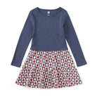 A girls' long-sleeve dress with a solid navy blue top and a tiered skirt featuring a repeating apple print on a navy and cream background.