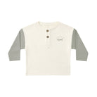 A children's long-sleeve henley shirt in off-white with sage green sleeves, featuring a three-button placket and a small 'stay wild' graphic on the left chest, displayed on a clean white background.
