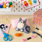 Crafting materials including a cat-shaped felt toy, scissors, yarn, and craft supplies on a table.