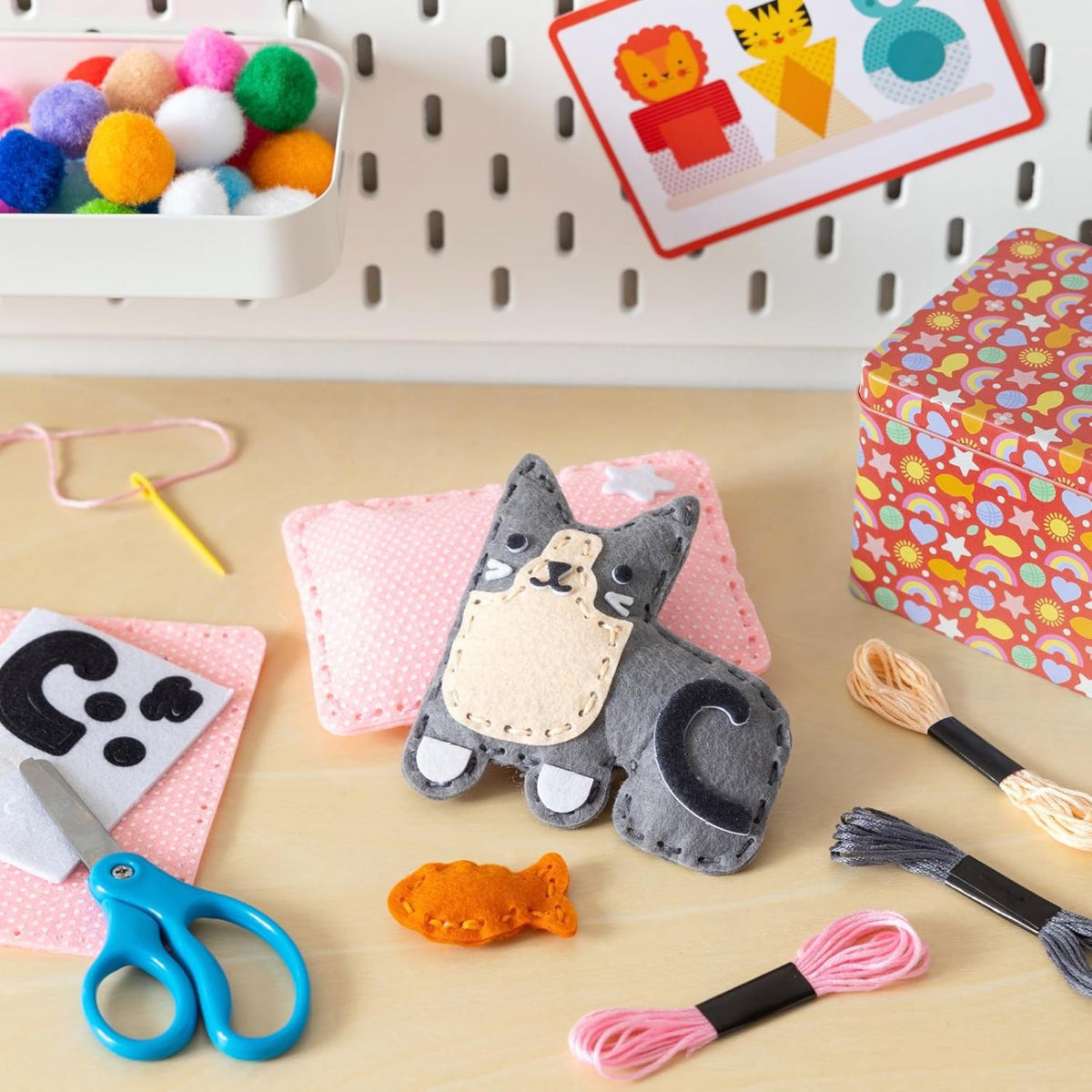 Crafting materials including a cat-shaped felt toy, scissors, yarn, and craft supplies on a table.