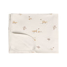 A folded cream-colored baby blanket featuring a delicate print of woodland animals, including foxes, rabbits, and leaves, on a solid white background.