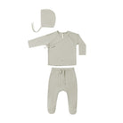 A three-piece baby clothing set in a light oatmeal beige color, including a long-sleeve wrap-style top, matching footed pants with a drawstring, and a bonnet with a tie, laid out on a solid white background.