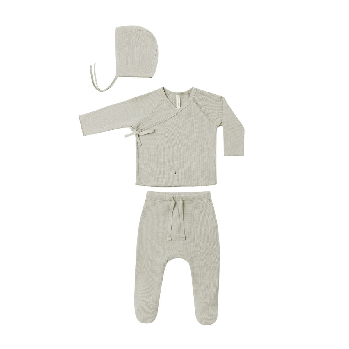 A three-piece baby clothing set in a light oatmeal beige color, including a long-sleeve wrap-style top, matching footed pants with a drawstring, and a bonnet with a tie, laid out on a solid white background.