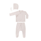 A three-piece baby clothing set in a soft, pale blush pink, including a long-sleeve wrap-style top with ruffle trim, matching footed pants with a drawstring, and a bonnet with ties, laid out on a solid white background.