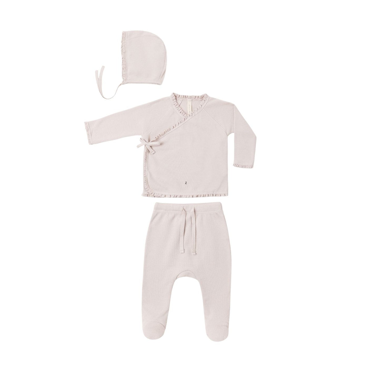 A three-piece baby clothing set in a soft, pale blush pink, including a long-sleeve wrap-style top with ruffle trim, matching footed pants with a drawstring, and a bonnet with ties, laid out on a solid white background.