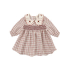 Quincy Mae long-sleeve baby dress in a red and white Christmas plaid pattern, featuring a scalloped white collar with delicate embroidery, a smocked front bodice, and ruffle trim.