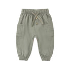 Front view of the Luca Pant - Spruce by Quincy Mae, featuring a sage green corduroy fabric, an elastic waistband with a matching adjustable drawstring, decorative front buttons, side patch pockets, and elasticized leg cuffs.