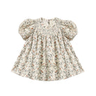 Carina Dress - Holiday Floral by Quincy Mae featuring a festive floral print on a natural hue, designed with a babydoll silhouette, short bubble sleeves, and diamond smocking around the neckline.