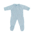 A light blue hand-knit baby jumpsuit for doll with a textured openwork pattern on the chest, raglan sleeves, and ribbed cuffs on the legs, shown against a plain white background.