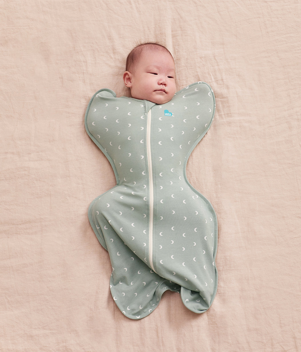 Newborn baby wrapped in a gray swaddle with white patterns on a pink blanket