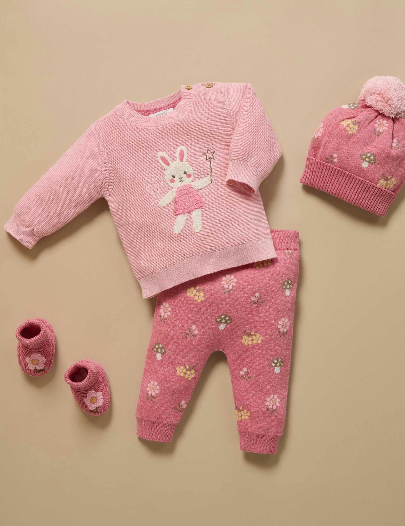 Pink baby outfit with sweater, pants, hat, and shoes on a beige background
