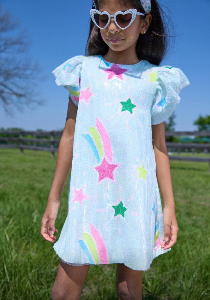 Young girl wearing a light blue dress with colorful star and rainbow patterns outdoors.