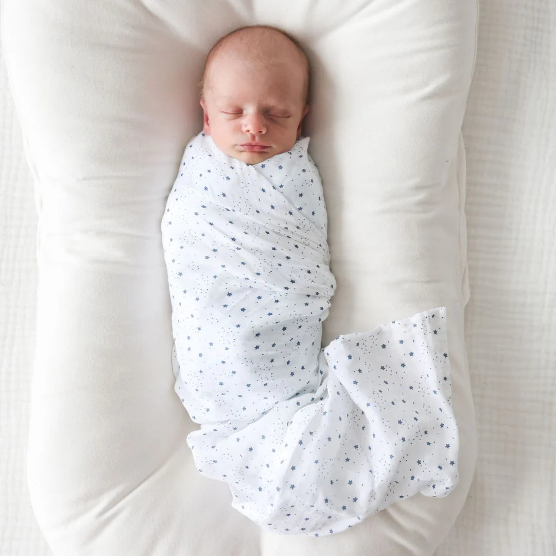 Newborn baby swaddled in a white blanket with black dots on a white background