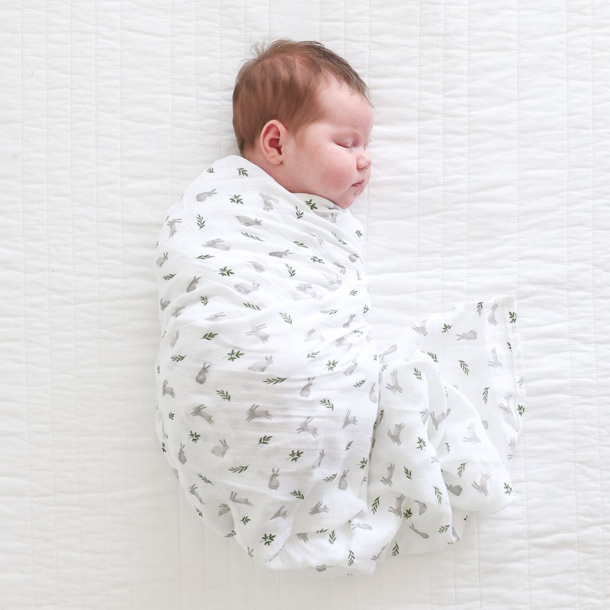 Newborn baby swaddled in a white blanket with small patterns on a white textured surface