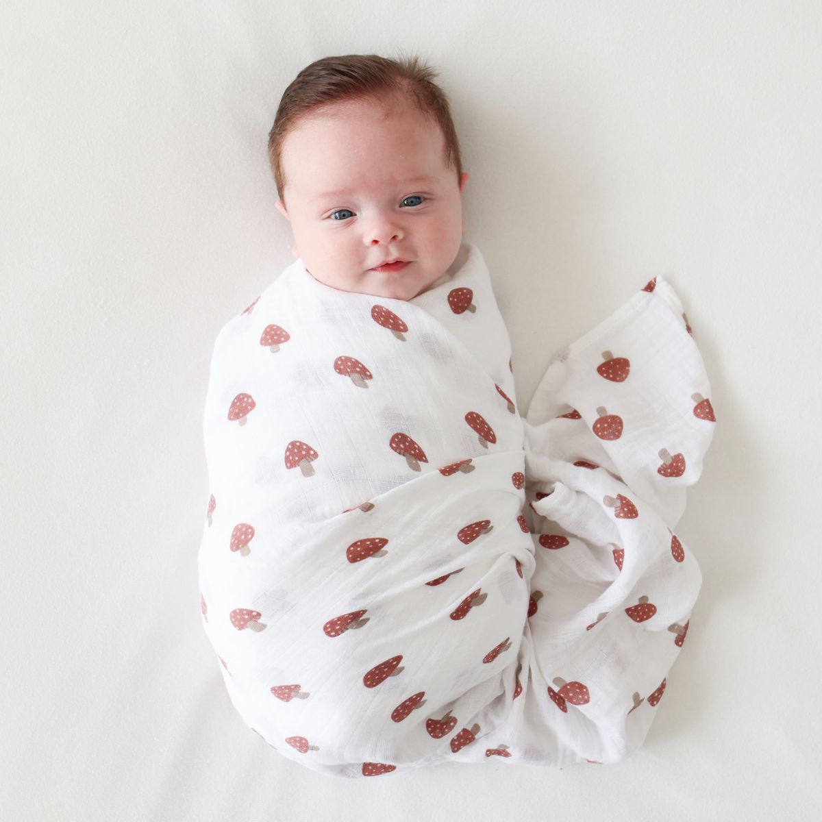 Newborn baby wrapped in a white blanket with red mushroom pattern on a light background