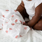 Person sitting on a bed with strawberry-patterned white blanket
