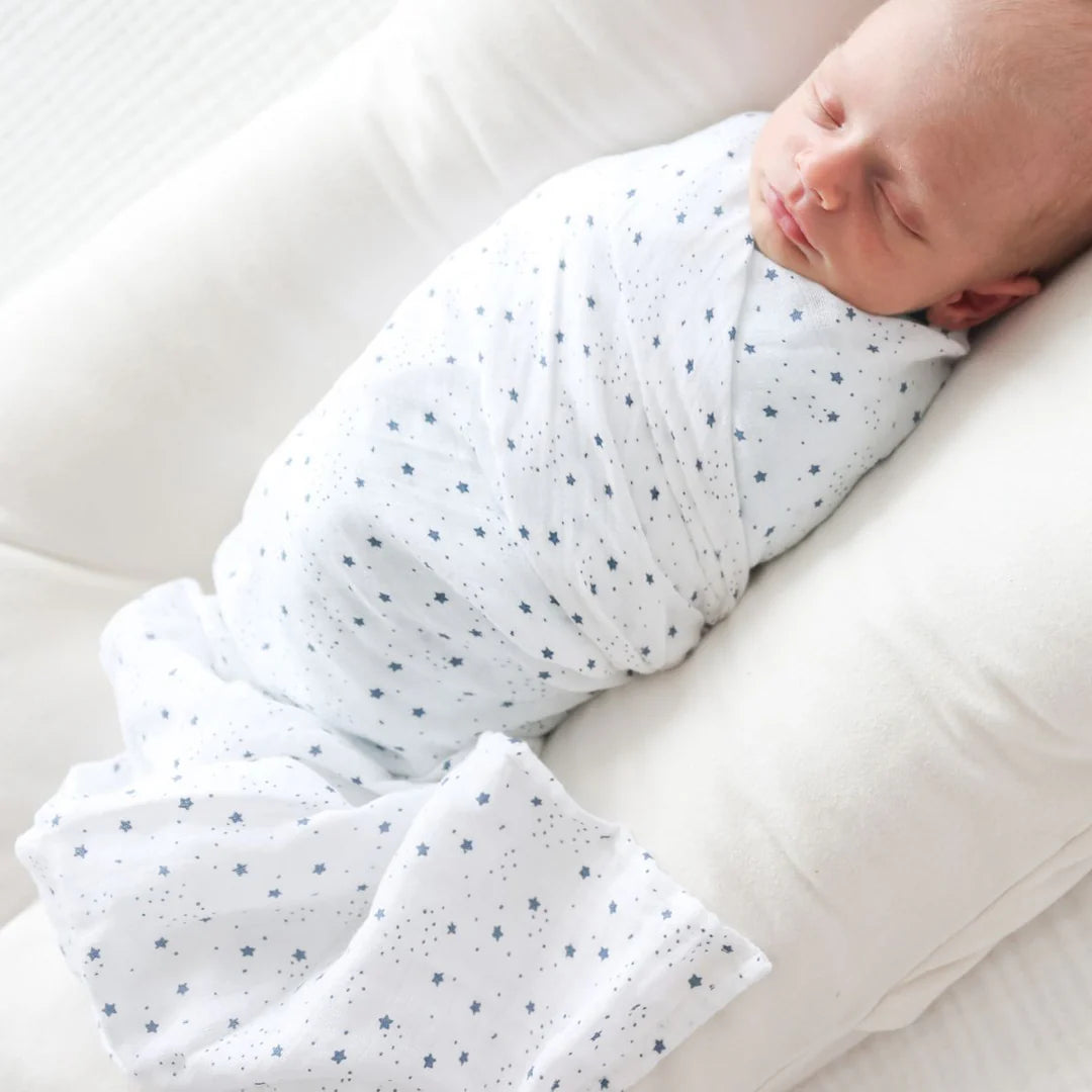 Newborn baby swaddled in a white blanket with blue dots, lying on a white surface.