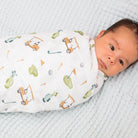 Newborn baby swaddled in a white blanket with golf-themed design on a textured surface.
