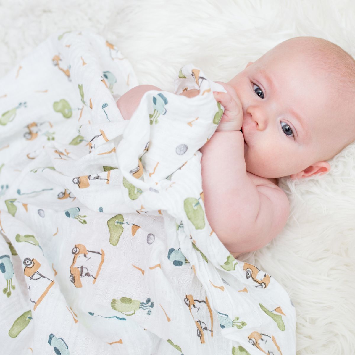 Baby wrapped in a colorful blanket with animal patterns on a white surface