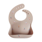 Beige silicone bib with colorful rocket designs on a white background