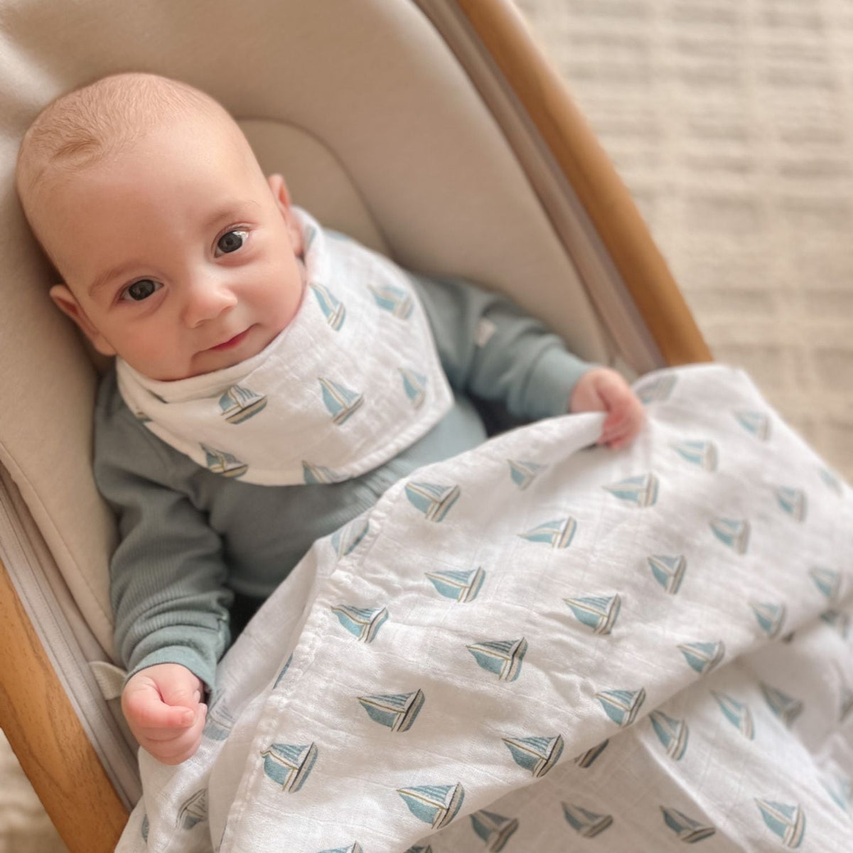 Baby wrapped in a blanket with sailboat pattern, sitting in a crib.