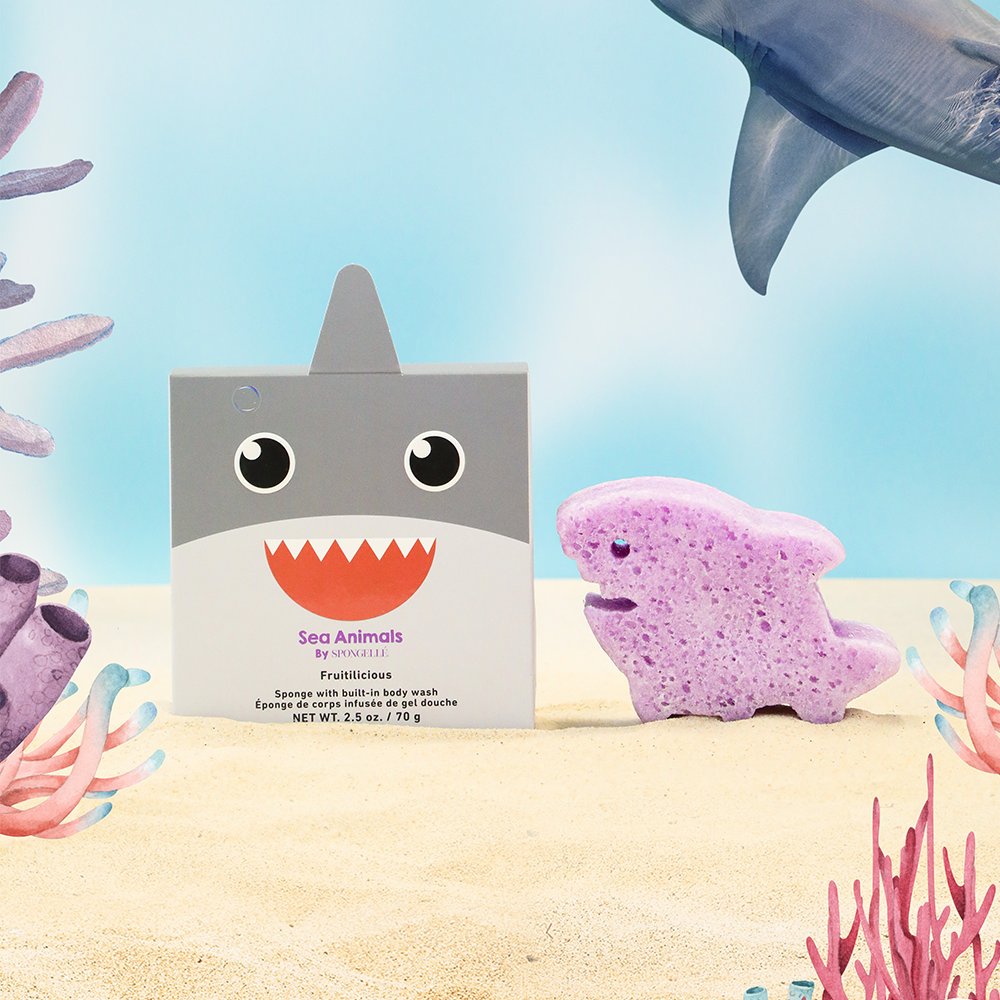 Shark-themed bath product packaging with a purple shark-shaped sponge on a beach background.