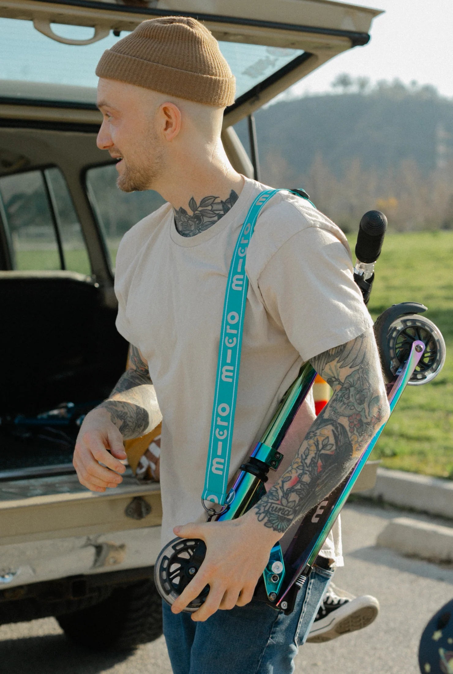 Man holding a skateboard with a tattooed arm, standing next to an open car trunk.